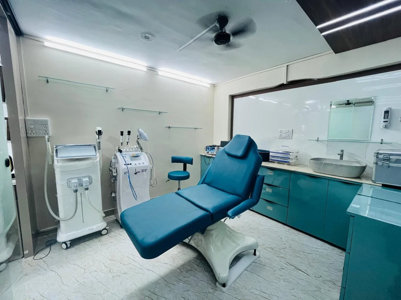 Advanced dermatology procedure room equipped with a blue examination couch and modern laser skin care devices.